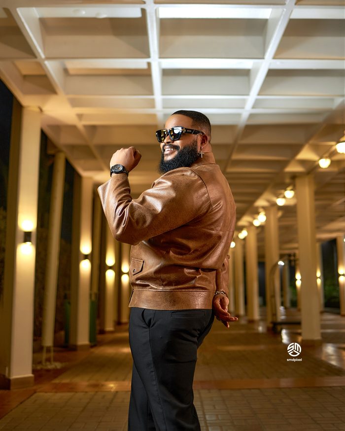 Whitemoney in a brown leather jacket in a warmly lit colonnade at night
