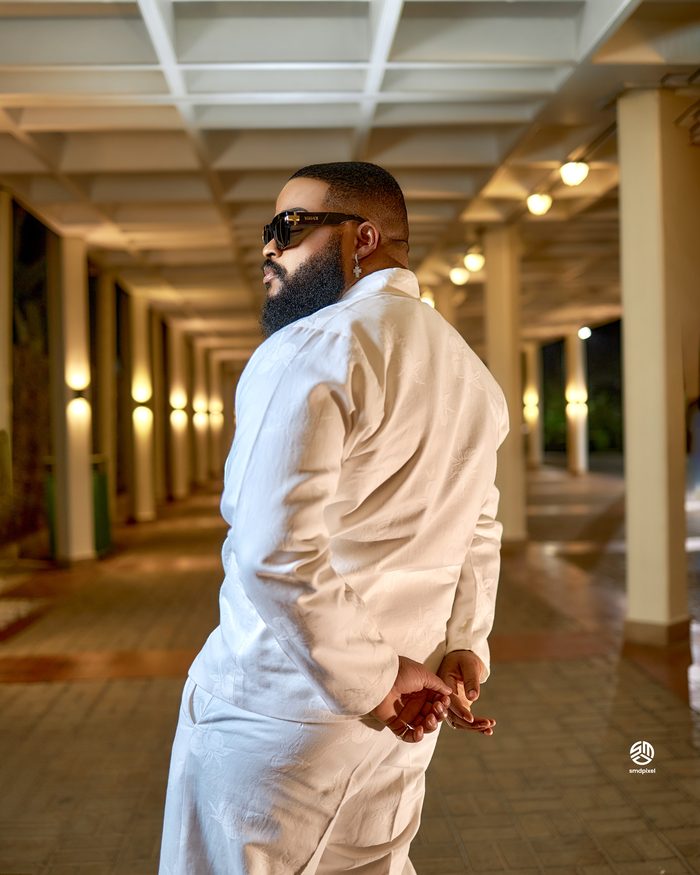 Whitemoney in a cream two-piece, turned away, in a lit colonnade