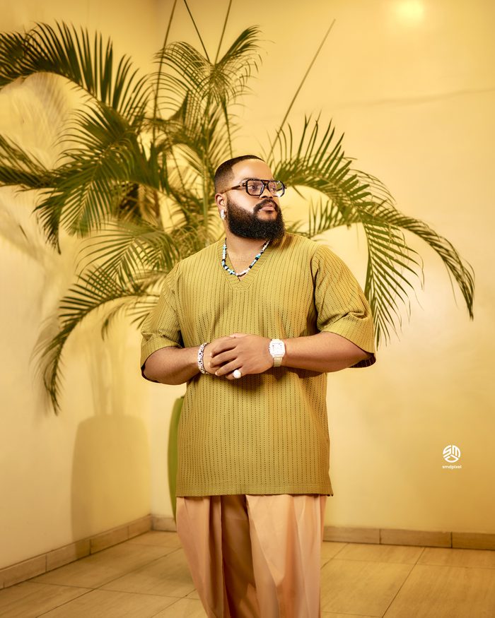 Whitemoney in an olive knit set in front of palm fronds