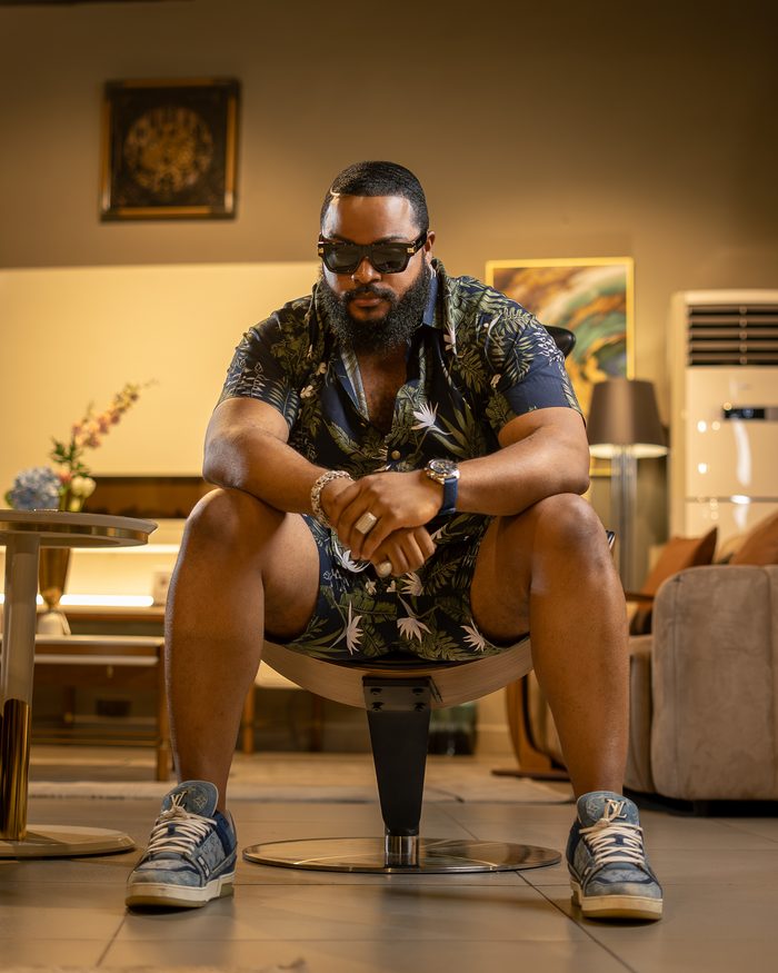 Whitemoney seated in a botanical shirt and trainers