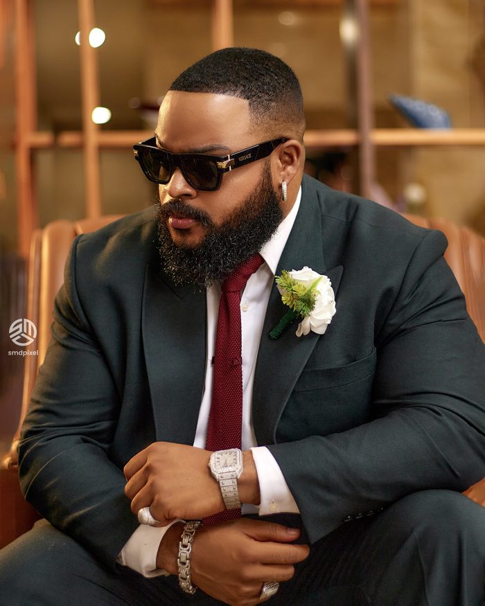 Whitemoney in a charcoal suit adjusting his cuff
